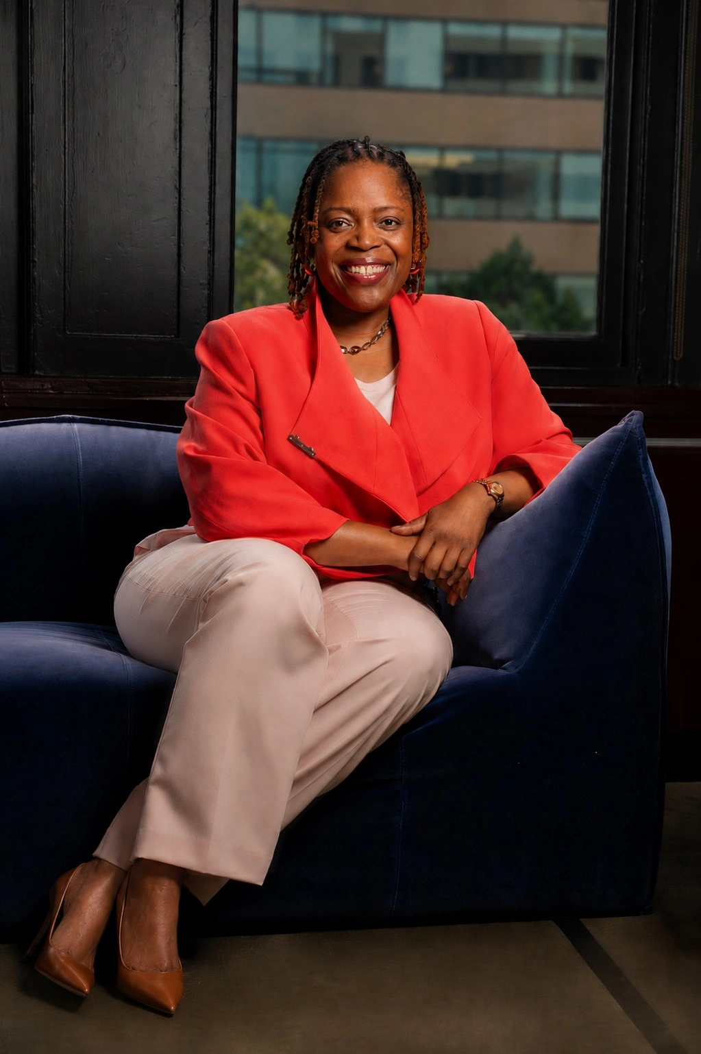 Janelle seated on a blue couch in a coral jacket